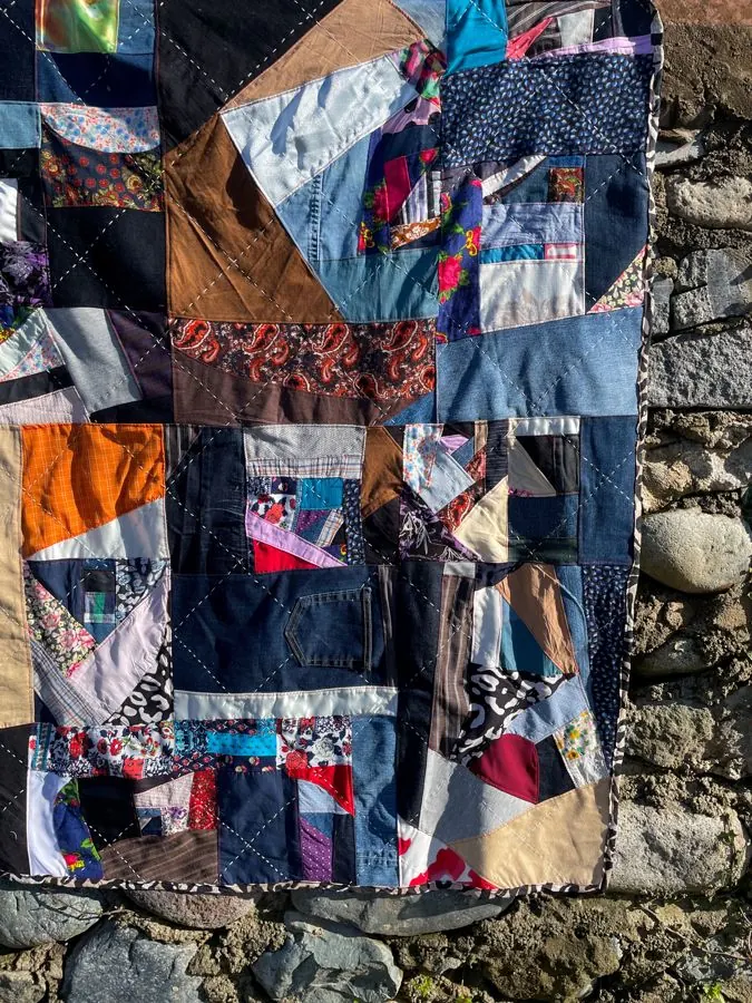 Patchwork quilt with vibrant patterns on an outdoor stone wall background.